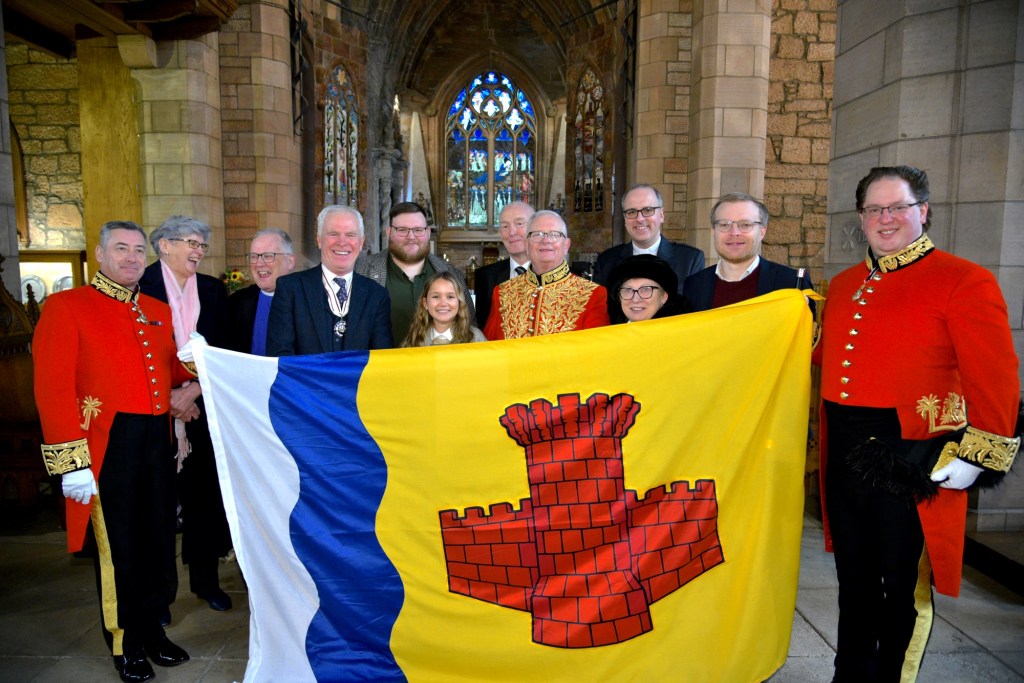 Flag held up by a Lyon officer either side. Standing behind it is the flag designer Ava (11yo) and various dignitaries.